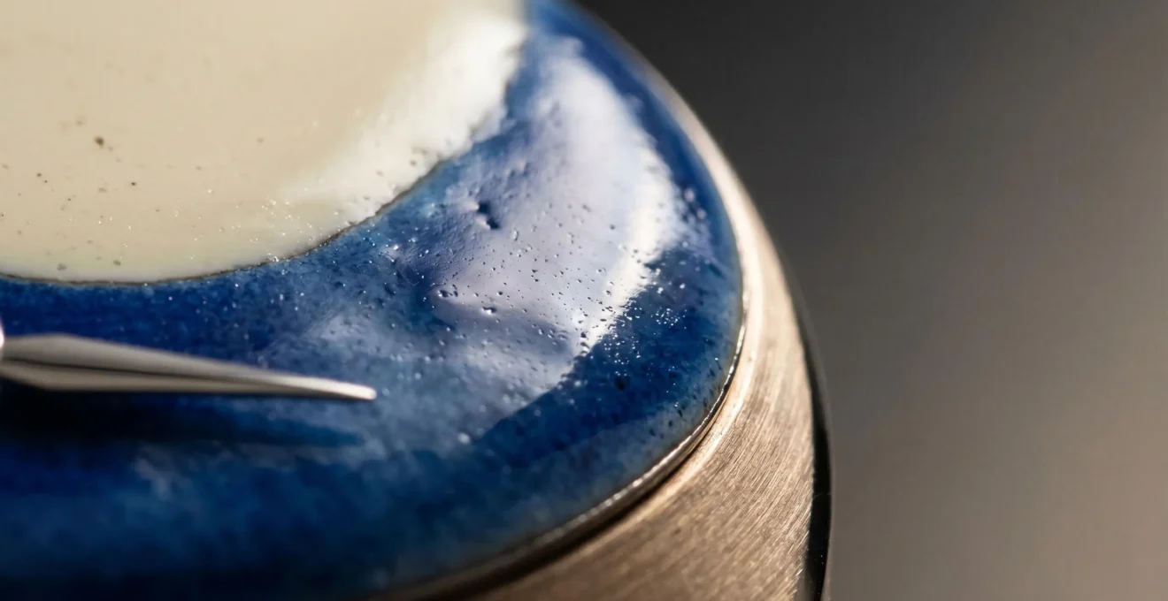 Gros plan d'un cadran de montre en émail Grand Feu artisanal suisse, révélant la profondeur vitrifiée et les reflets lumineux caractéristiques de cette technique ancestrale