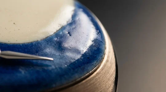 Gros plan d'un cadran de montre en émail Grand Feu artisanal suisse, révélant la profondeur vitrifiée et les reflets lumineux caractéristiques de cette technique ancestrale